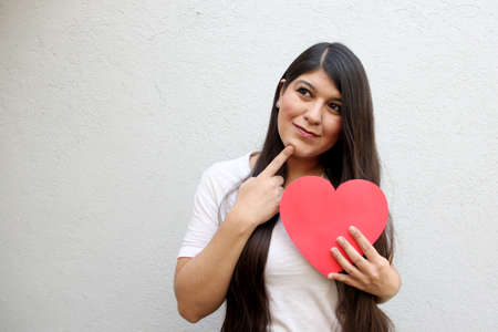 Latin adult woman with a big red heart shows her enthusiasm for the arrival of February and celebrate Valentine's Day of Love and Friendship with her family, partner and friends with joy and affectionの写真素材