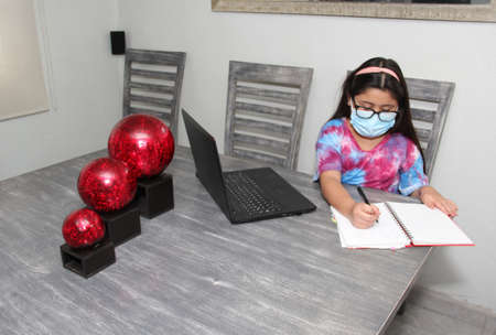 Little Hispanic girl doing school at home with glasses and face masks due to the quarantine of the Covid-19 pandemic due to coronavirus protectionの写真素材