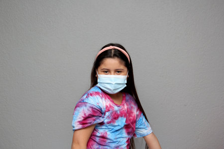 Happy Latin Little Girl Wearing Face Masks To Protect Herself From Coronavirus In The New Normal Due To The Covid-19 Pandemicの写真素材