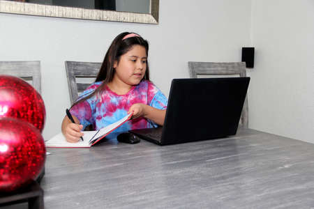 Little Hispanic girl doing school at home with glasses and face masks due to the quarantine of the Covid-19 pandemic due to coronavirus protectionの写真素材