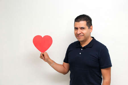 Latin adult man with a big red heart shows his enthusiasm for the arrival of February and celebrate...