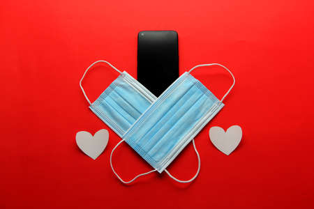 Valentine's Day in pandemic by covid-19, mobile phone with protection mask clinical use and pink heartsの写真素材