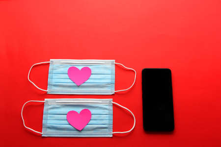 Valentine's Day in pandemic by covid-19, mobile phone with protection mask clinical use and pink heartsの写真素材