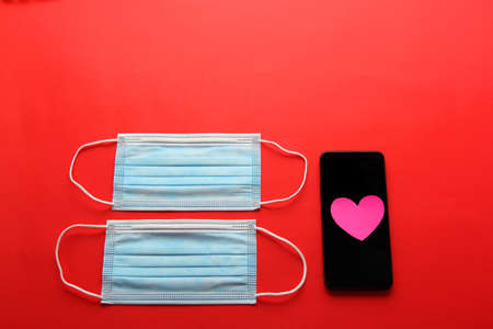 Valentine's Day in pandemic by covid-19, mobile phone with protection mask clinical use and pink heartsの写真素材