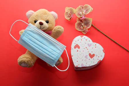 Valentine's Day in pendemic for covid-19, teddy bear, box of chocolates, flowers and hearts with protection mask clinical useの写真素材