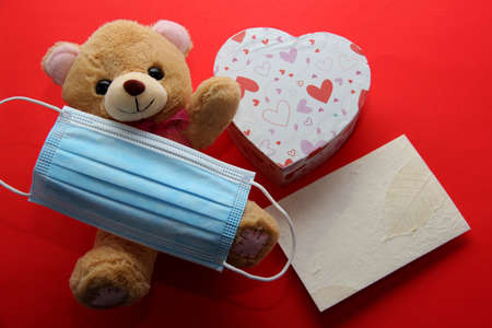Valentine's Day in pendemic for covid-19, teddy bear, box of chocolates, flowers and hearts with protection mask clinical useの写真素材