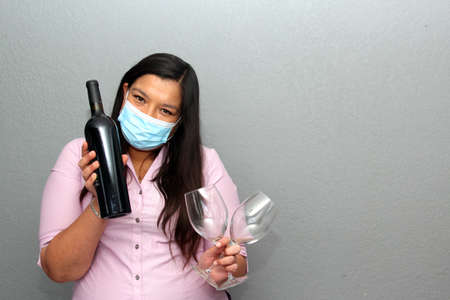 Valentine's day in contingency covid-19. Latin woman with protection mask and red wine and chocolate as a giftの写真素材