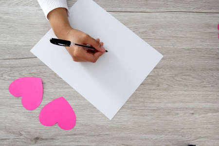 Valentine's Day. heart in female hands writing love letter, vintage wooden background for advertising banerの写真素材