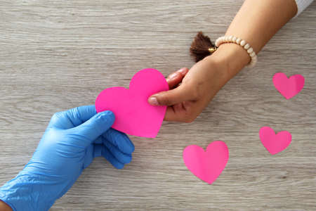 Valentine's Day. heart in the hands of doctor with latex gloves and female, vintage wooden...