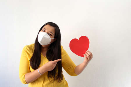 Latin adult woman with a yellow blouse and a big red heart shows her enthusiasm for Valentine's Day...