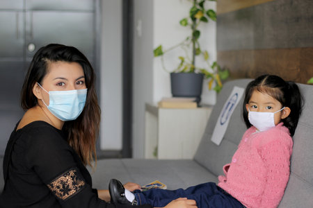 Latin mom with 2-year-old girl putting on protective face masks for new normality covid-19の写真素材