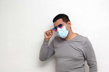 Latin adult man with face mask and heart-shaped glasses excited for February Valentine's Day of Love and Friendship in the new normality due to the Covid-19 pandemicの写真素材