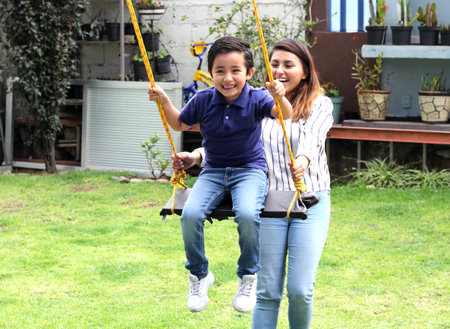 Latina woman mom and 6 year old boy, playing swing in the gardenの写真素材