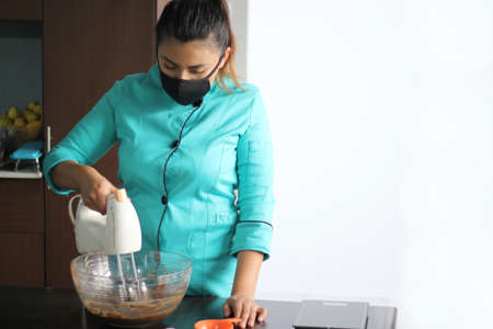 Latin woman chef with black protection mask, preparing cake flour with kitchen utensils, new normal...
