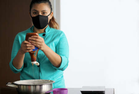 Latin woman chef with black protection mask, preparing cake flour with kitchen utensils, new normal...