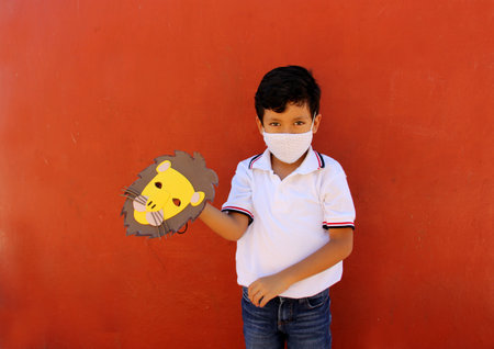 Latin little boy in uniform shirt proudly and happily shows the lion mask he made for school...