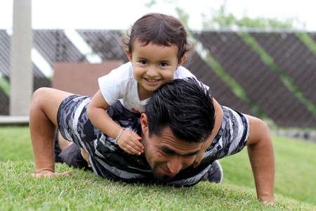 Latino dad with 3-year-old girl playing on the park lawnの写真素材