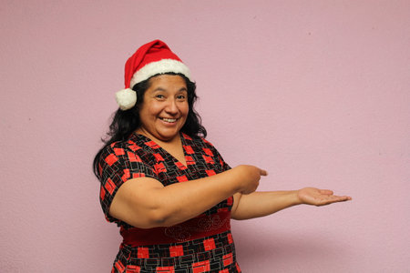 Fat latin adult woman on overweight bodypostive on Santa hat shows her enthusiasm for the arrival of December and celebrating Christmasの写真素材