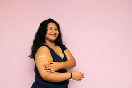 Young body-positive black-haired Latina woman shows her newly vaccinated arm against Covid-19 in the new normal for the oronavirus pandemicの写真素材