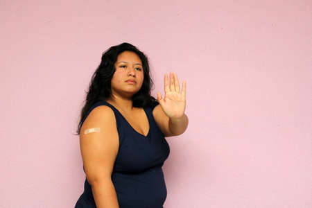 Young body-positive black-haired Latina woman shows her newly vaccinated arm against Covid-19 in the new normal for the oronavirus pandemicの写真素材