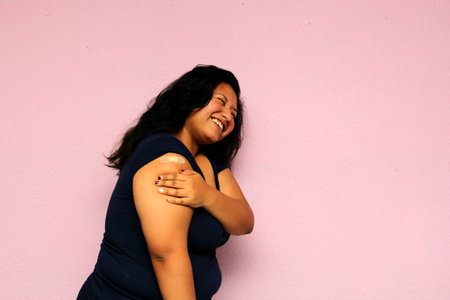 Young body-positive black-haired Latina woman shows her newly vaccinated arm against Covid-19 in the new normal for the oronavirus pandemicの写真素材