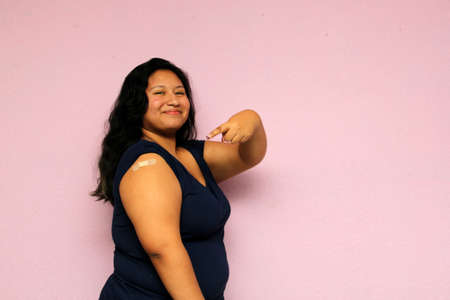 Young body-positive black-haired Latina woman shows her newly vaccinated arm against Covid-19 in the new normal for the oronavirus pandemicの写真素材