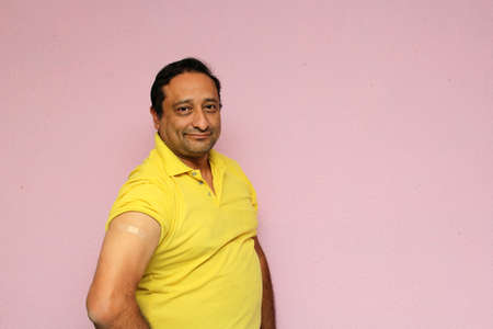 Latino mature adult man shows his arm recently vaccinated with plaster against Covid-19 in the new...