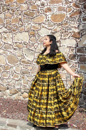 Young Latina teenager woman wears a traditional embroidered yellow and black Mexican regional dress from the state of Chiapas Mexico happy and proud of her culture and traditionsの写真素材
