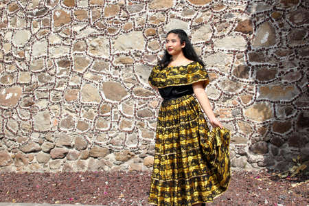 Young Latina teenager woman wears a traditional embroidered yellow and black Mexican regional dress from the state of Chiapas Mexico happy and proud of her culture and traditionsの写真素材