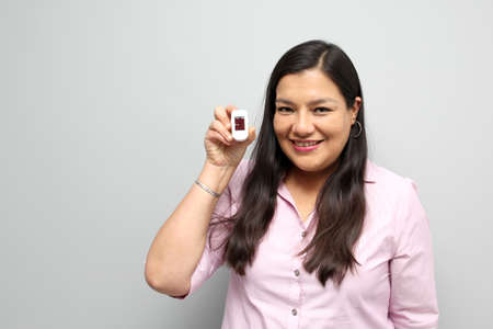 Latin adult woman with dark brown hair shows in her hand an oximeter on her finger that measures her...