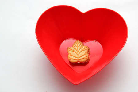 Delicious cookies filled with vanilla cream made with honey or maple syrup from Canadian trees, the traditional sweet of Canada in a red bowl of heart shapeの写真素材