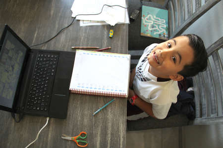 back to school, 7 year old Latino boy in online home classes with laptop and school supplies