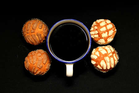 Fresh, delicious and fluffy Mexican bread Manteconchas cupake type vanilla and chocolate flavor accompanied by coffee on a black background traditional of the culture of Mexicoの写真素材