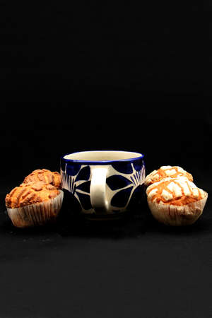 Fresh, delicious and fluffy Mexican bread Manteconchas cupake type vanilla and chocolate flavor accompanied by coffee on a black background traditional of the culture of Mexicoの写真素材