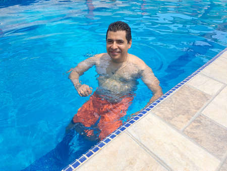 Latino adult man swims in the pool during his summer vacation or weekend uses sunscreen as a skin...