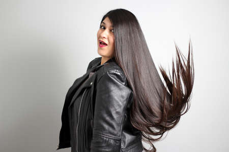 Latin adult real woman with long straight black hair that flies in the air is content and happy with...