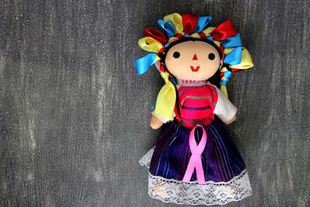 Mexican handmade doll with pink ribbon on vintage gray wooden background for campaign against breast cancerの写真素材