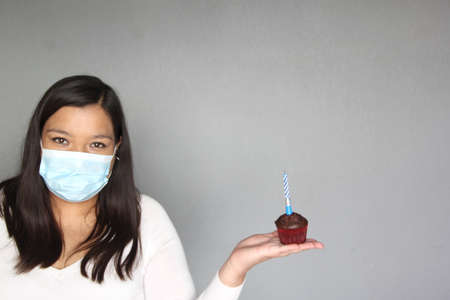 latin woman with black hair with protection mask, celebrates birthday with cake at home due to...