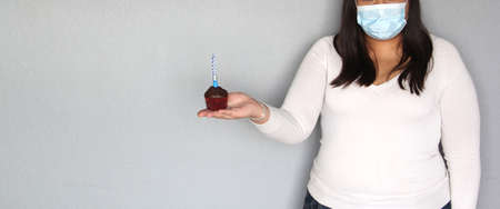latin woman with black hair with protection mask, celebrates birthday with cake at home due to...