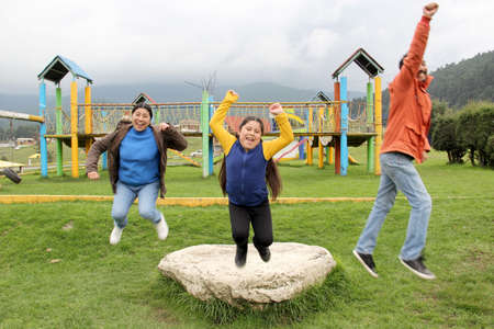 Latin family of dad, mom and daughter enjoy a picnic flying a kite and jumping with happiness for...