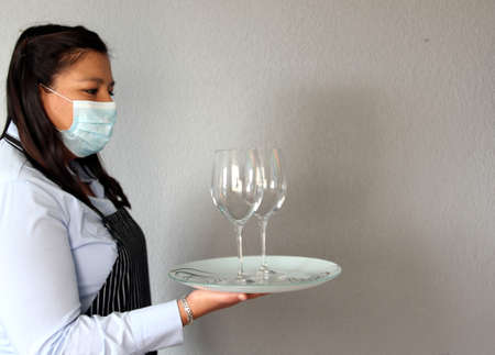 Latin woman sommelier with red wine, crystal glasses working with protection mask and latex gloves, new normal covid-19の写真素材