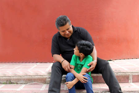 Single latino grandfather and grandchild play and have fun together spending quality family time on Father's Day celebrating victory with hugs and kissesの写真素材