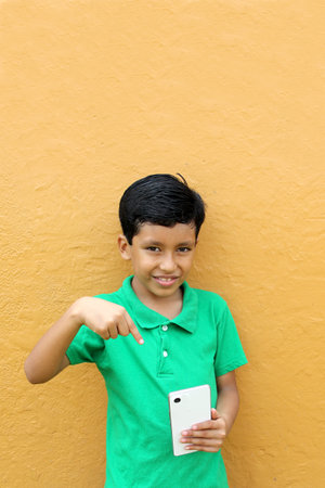 Latin child boy over isolated yellow background with cell phone in victory position shows happy and excitedの写真素材