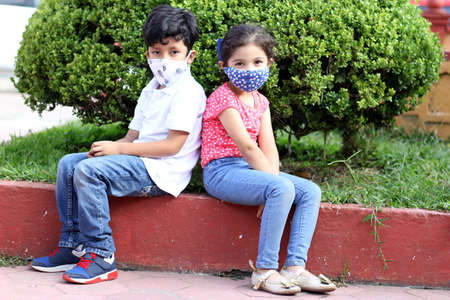 6-year-old boy and girl with protective masks for the covid-19 virus, sitting in the park, new normalの写真素材