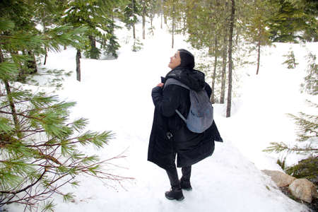 Latin adult woman with black jacket and gray backpack hiking in the snowy mountain very happy, free,...