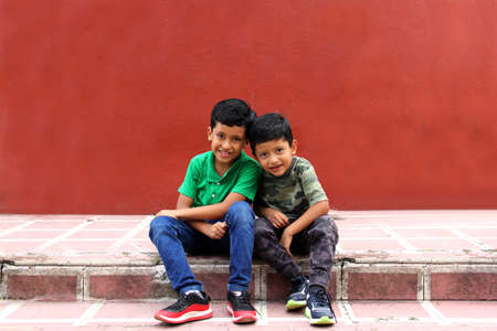 Two dark-haired Latino male children sitting on the ground in a park living in poverty without toys, dream, play, imagine a happy childhoodの写真素材