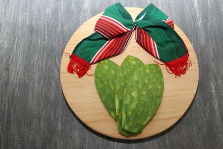 Festive Mexican objects: handmade doll and tricolor tie bow next to nopales, typical Mexican food on a cutting boardの写真素材