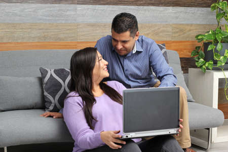Latino adult man and woman couple use their laptop in the living room to shop online, make payments, plan trips, view photos and make video callsの写真素材