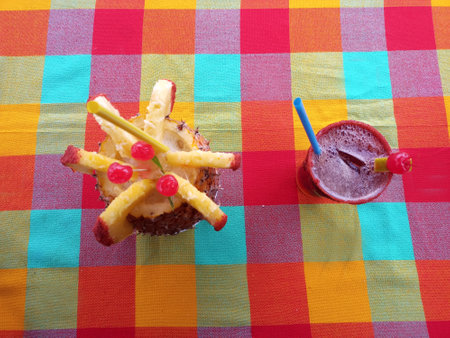 Refreshing drinks on a table with a colorful tablecloth is a pia colada and a michelada with a straw...