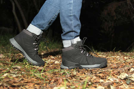 Legs of a woman with denim pants and black hiking boots walking alone in the forest as part of the...